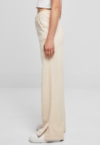 Beige sweatpants med elastisk midje, sidelommer og sidespalter. Laget av myk stoff, med en avslappet passform og diskret søm.