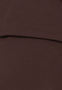 Tessuto di cotone marrone con una texture a coste. Il materiale presenta una finitura liscia, con un orlo pulito lungo i bordi. Nessun motivo o accento visibili.