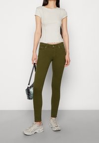 Olivově zelené strečové džíny s úzkým střihem, předními kapsami a zipem. Kombinované se světle béžovým žebrovaným tričkem s krátkým rukávem a světle kopačkami.