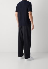 Men's navy T-shirt with short sleeves paired with black pinstriped trousers and white sneakers. Fabric appears smooth, and trousers are loose-fitting.