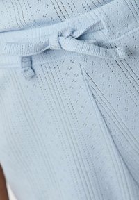 Gaiši zils adīts audums ar mazām perforācijām un sasietu jostasvietu ar tekstūru. Dizains ietver vertikālas svītras un brīvu piegriezumu.