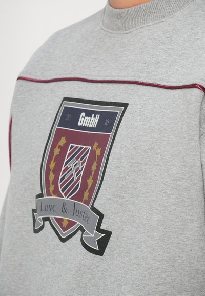 Felpa grigia con un'emblema grafico che presenta uno scudo bordeaux, dettagli dorati e il testo "Amore e Giustizia" su un nastro.