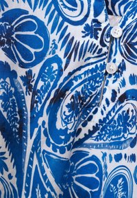 Tela de algodón con un patrón de paisley en azul y blanco, con diseños intrincados y tres botones blancos en el cuello.