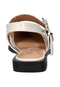 Witte lakleren sandalen met een vlakke zwarte zool, verstelbare gespstrap en beige gevoerde binnenzool. Maatlabel zichtbaar van binnen.