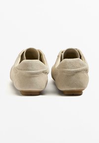 Beige mokkasiner med rund tå og lav hæl, med en glat søm langs kanten og en struktureret overflade.