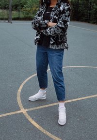 Black and white patterned puffer jacket, black top, blue jeans, and white high-top sneakers, set on a gray basketball court.