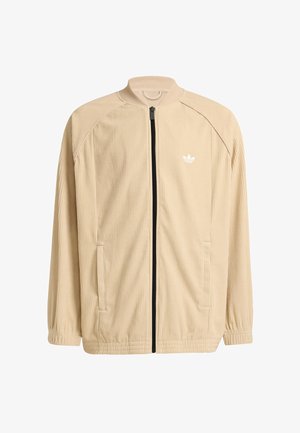 Giacca in velluto a coste beige con chiusura a zip nera, colletto alto e logo bianco sul petto sinistro. Presenta polsini elastici e tasche laterali.