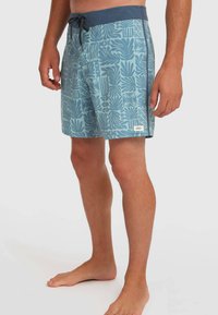 Shorts de bain pour hommes en bleu clair avec un cordon de serrage bleu foncé. Ornés d'un motif de feuillage tropical et d'une petite étiquette sur le côté.