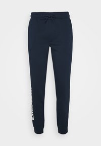 Navy blue joggers made of soft cotton blend fabric, featuring a drawstring waist, cuffed ankles, and a white logo printed on the side.