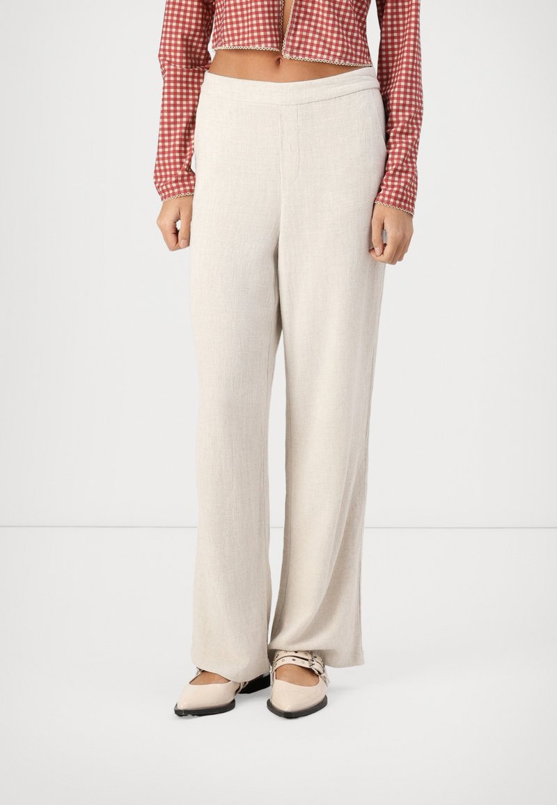 Pantalones de pierna ancha en color beige claro, confeccionados en un tejido suave y texturizado, con una cinturilla plana y longitud completa. Combínalos con zapatos planos de color crema.