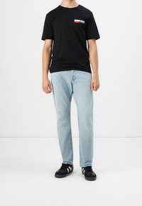 Camiseta de algodón negra con un pequeño logo impreso, combinada con unos jeans de pierna recta de color azul claro y zapatillas negras con rayas blancas.