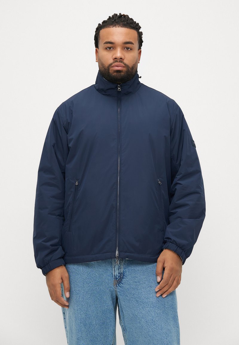 Geacă căptușită de culoare albastru marin, cu guler înalt, fermoar frontal și manșete elastice. Țesătură ușoară cu textură netedă și buzunare laterale.