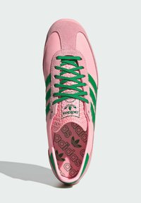 Sapatilha desportiva rosa com riscas verdes, materiais em camurça e malha, biqueira redonda, língua texturizada e palmilha estampada com logotipo.