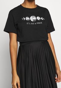 Svart bomull t-shirt med ett grafiskt tryck av månens faser och texten "DET ÄR BARA EN FAS" i vitt. Enkel rund hals och avslappnad passform.