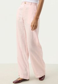 Světlé růžové lněné kalhoty s širokým střihem, se zapínáním na přední knoflík a hladkou texturou, doplněné hnědými balerínami.