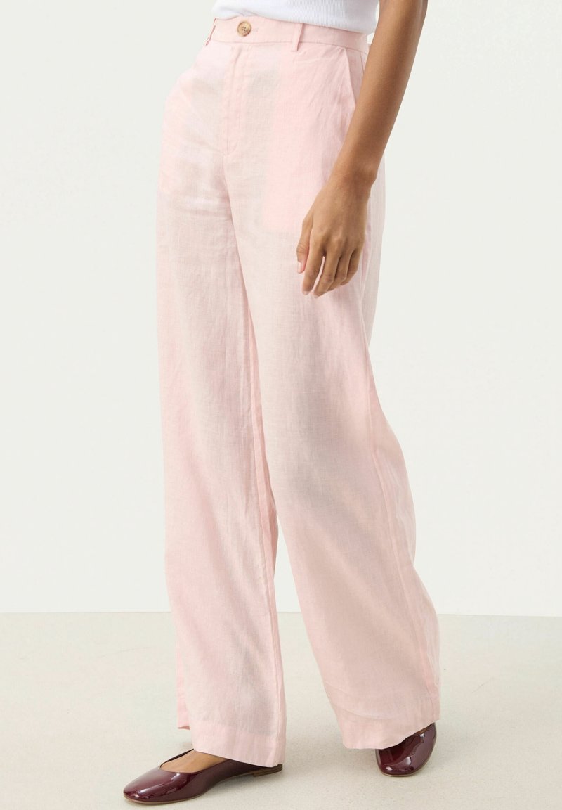 Světlé růžové lněné kalhoty s širokým střihem, se zapínáním na přední knoflík a hladkou texturou, doplněné hnědými balerínami.