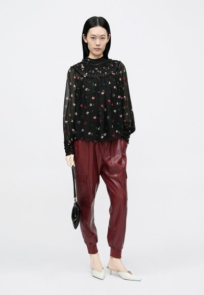 Blusa nera a fiori con colletto arricciato, abbinata a pantaloni cargo in pelle bordeaux e sabot con tacco chiaro. Borsa nera come dettaglio.