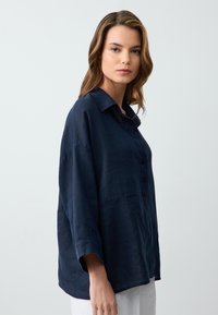 Camicia azzurra button-up realizzata in lino; presenta un colletto, spalle scese e una vestibilità rilassata. Tessuto morbido e design minimale.