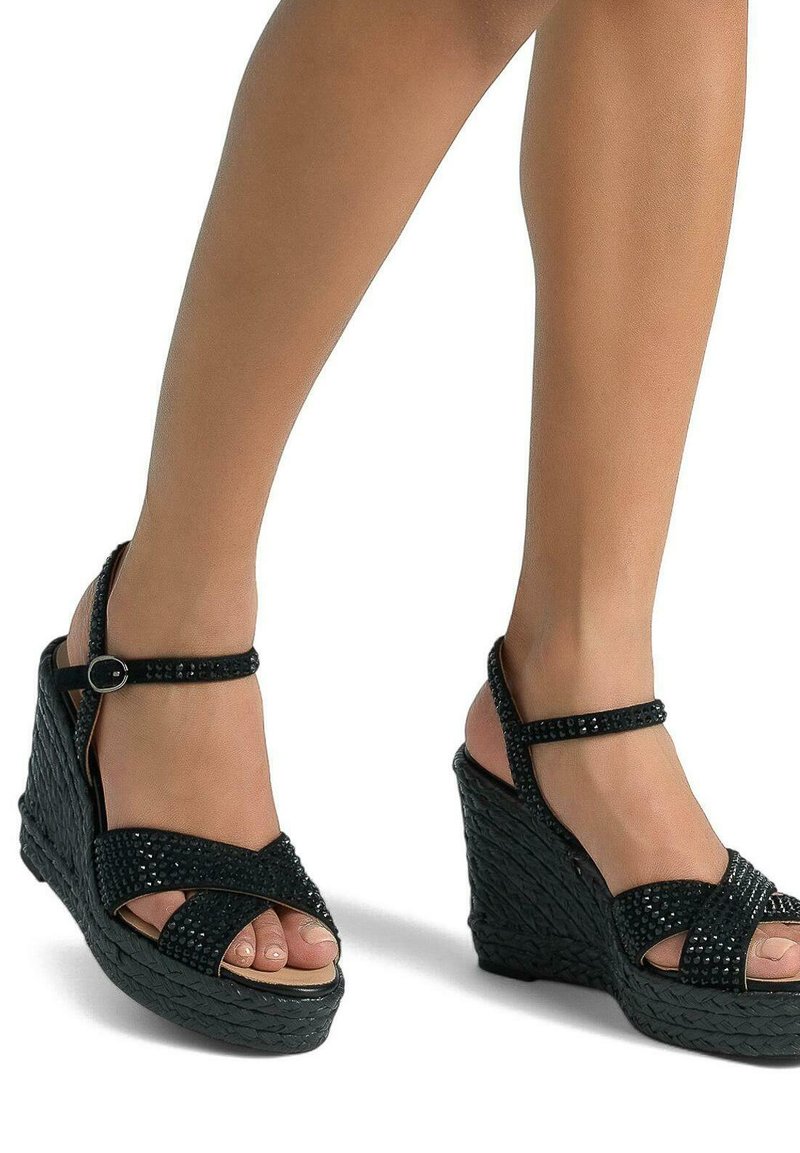 Sandales compensées noires avec une texture tissée, des rhinestones décoratifs et une fine bride au cheville. Le design ouvert laisse entrevoir les orteils.