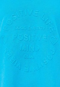 Pullover in cotone turchese con testo embossato: "VITA POSITIVA, ENERGIA BUONA, MENTE POSITIVA, CLUB" con accenti a forma di cuore.