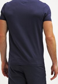 T-shirt a maniche corte blu scuro con una texture liscia e scollo a V. Presenta un design aderente e cuciture sulle spalle.