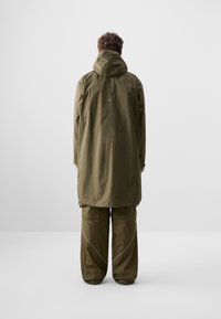 Olivgrüne wasserdichte Jacke mit Kapuze, im entspannten Schnitt und mit verstärkten Nähten. Kombiniert mit passenden, locker geschnittenen Hosen.