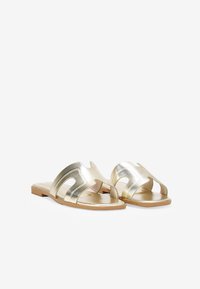 Sandalias deslizantes metálicas doradas con un diseño recortado, suela plana y textura suave. Presentan un estilo minimalista con una silueta simple.