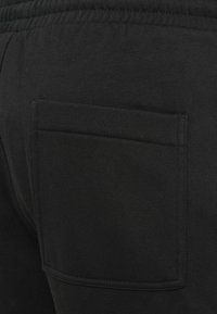 Schwarze Jogginghosen mit einer großen Gesäßtasche und erhöhten Nähten. Hergestellt aus weichem Stoff, mit einem elastischen Bund für mehr Komfort.