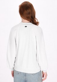 Hvid pullover sweatshirt med en tekstureret overflade, raglanærmer og ribbede manchetter. Har et lille sort logo på det bagerste halsudskæring.