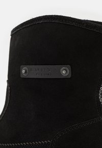 Stivale in suede nero con cuciture rinforzate, dotato di un'etichetta metallica rettangolare con "LUHTA EST 1907" e chiusure tonde sui lati.