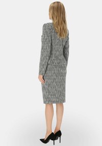 Szary kostium z tkaniny typu tweed o dopasowanym kroju, z długimi rękawami i spódnicą do kolan. W zestawie czarne szpilki. Widoczna faktura tkaniny.