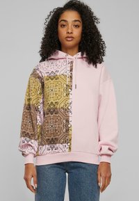 Hettegenser med rosa stoff på den ene siden og et m�ønstret brunt-gull trykk på den andre. Myk tekstur med ribbestrikkede mansjetter og kant. 