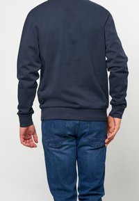 Marinblå sweatshirt med långa ärmar och ribbade muddarna, i kombination med blå denimjeans. Enkel, enfärgad design med en figurnära silhuett.