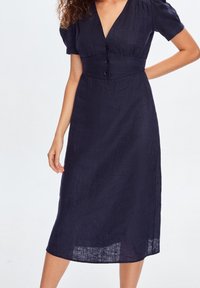 Abito in lino navy con scollatura a V, maniche corte e corpino aderente con tre bottoni frontali. Lunghezza midi e tessuto con texture.