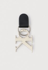 Metallic sølv nøglering med abstrakt geometrisk design fastgjort til en sort læderløkke og sølv ringe på ensfarvet baggrund.