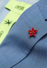 Blue fabric blazer with a textured finish, featuring a red floral lapel pin and a green fabric label with "CIRQUE" printed in black.