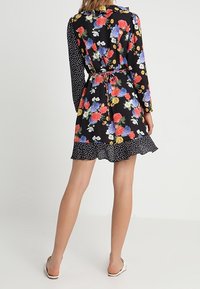 Vestido floral con fondo negro, rosas y tonos azules coloridos, mangas largas, un cuello con volantes y un dobladillo de falda con lunares.