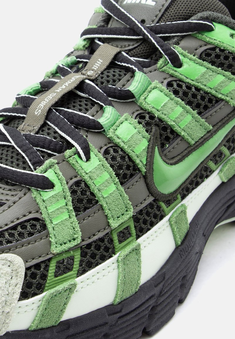 Gros plan sur une chaussure de sport Nike noire et verte en tissu mesh, avec des superpositions en daim, des lacets noirs et une étiquette de languette marquée.