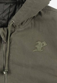 Oliwkowa kurtka zapinana na zamek, wykonana z teksturowanej tkaniny, z podszewkowanym kapturem, regulowanymi sznurkami oraz wyszywanym logo w dopasowanym kolorze.