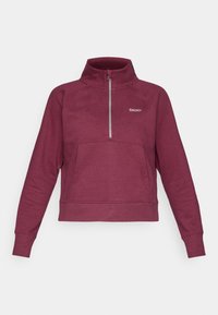 Burgundy pulóver, magas gallérral, félig zipzárral elöl és elülső zsebből készült. Puha anyagból készült, bordázott mandzsettákkal és aljjal.