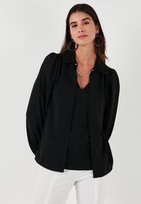 Black blouse with a collared neckline, puffed sleeves, and a relaxed fit, paired with white pants. Smooth texture, minimal detailing.