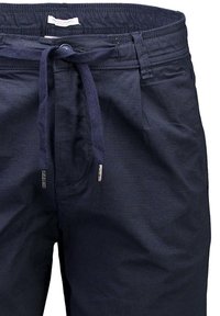 Dunkelblaue Hosen aus strukturiertem Stoff. Mit einem Kordelzugbund mit metallischen Enden. Enthält einen vorderen Knopfverschluss und dezente Nähte.