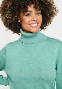 Tirkīza krāsas turtleneck džemperis ar teksturētu adījumu, ar ribotas piedurknes un apkakli; audums izskatās mīksts un silts.