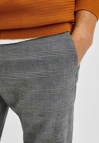 Gray plaid trousers featuring a check pattern with black and blue accents, made of textured fabric. The waistband is elasticized with a ribbed finish.