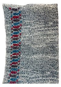 Tissu arbore des motifs texturés gris, blanc et noir, avec des accents colorés en rouge et bleu le long d'un bord, créant un contraste saisissant.