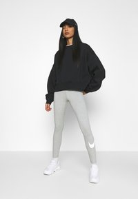 Felpa nera oversize, leggings grigi con logo Nike bianco e scarpe da ginnastica bianche. Il modello indossa un cappellino nero, con capelli lisci e lunghi.