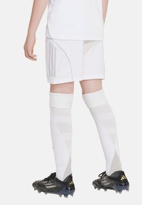 Weiße Sportshorts mit grauen Akzenten, kombiniert mit weißen Kompressionssocken mit texturiertem Muster und schwarzen Fußballschuhen.