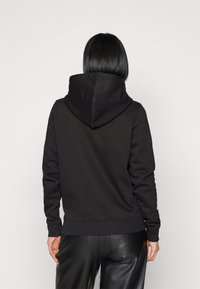 Sudadera negra con una textura suave, que cuenta con una gran capucha, puños acanalados y dobladillo inferior. Lleva puestas pantalones de cuero negros.