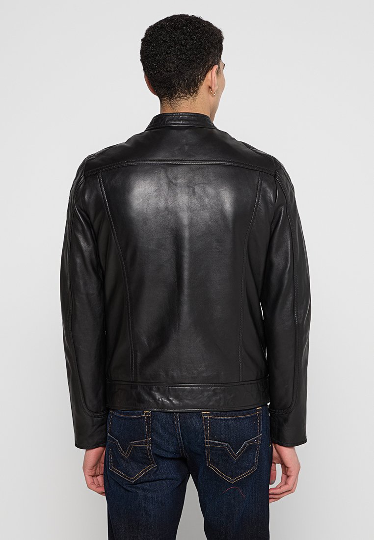 Chaqueta de cuero negro con una textura suave, que presenta un cuello clásico y costuras estructuradas, llevada sobre unos jeans de mezclilla oscura.