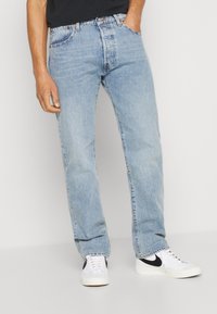 Jeans de mezclilla azul claro con un corte recto, diseño de cinco bolsillos y un ligero desvanecimiento, combinados con zapatillas blancas con acentos negros.